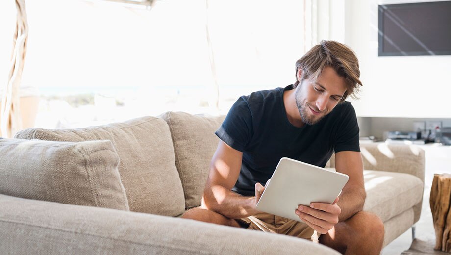 mężczyzna facet w salonie mieszkania siedzi na kanapie sofie I patrzy w tablet sprawdzając oferty hipotek