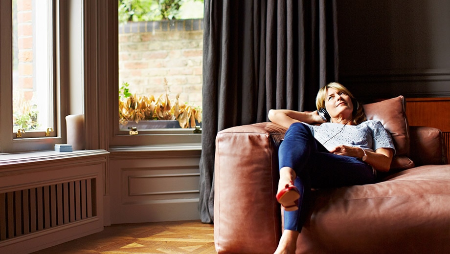kobieta blondynka siedzi na brązowej kanapie sofie ze słuchawkami na uszach głowie i słucha muzyki