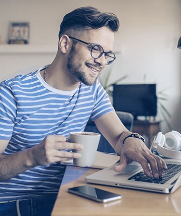 Klient Citibanku pijący kawę w swoim domu podczas składania wniosku o kredyt gotówkowy przez Internet na zakup nowego samochodu